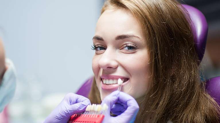 A woman comparing teeth color shades at the dentist Gaithersburg MD